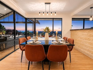 A modern dining area with a large table, chairs, and a view of the landscape.