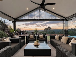 A modern outdoor lounge area with wicker furniture, a glass coffee table, and a ceiling fan.