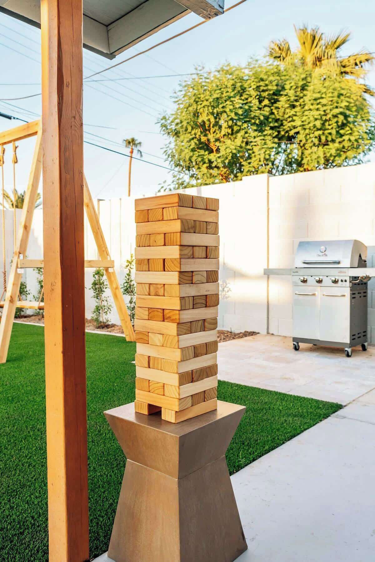 Una estructura de madera con una pila de bloques de madera sobre un pedestal, una parrilla y un conjunto de columpios al fondo.