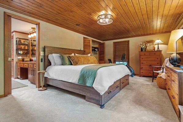 Een slaapkamer met een houten plafond, een bed met kussens, een dressoir en een lamp.