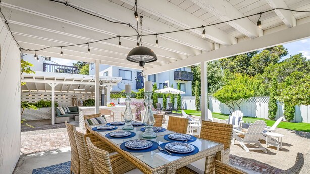 An outdoor patio with a glass-top table set for dining, surrounded by wicker chairs and a blue rug.