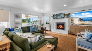 A spacious living room with a fireplace, green sofa, and a large TV displaying a beach scene.
