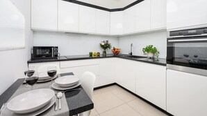 A modern kitchen with white cabinets, a black countertop, a microwave, an oven, and a dining table set with plates and glasses. - Lumina apart with parking in Center (Łódź)