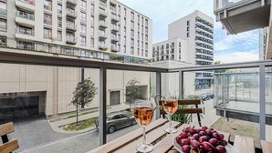 A balcony with a table, two glasses of wine, and a plate of grapes.