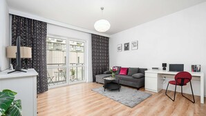A modern living room with a sofa, a desk, a chair, a coffee table, and a large window. - Lumina apart with parking in Center (Łódź)