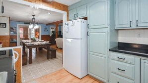 A kitchen with light blue cabinets, a white refrigerator, and a wooden dining table with chairs. - Spacious 6-bedroom home just steps from outdoor adventures! (Laconia)