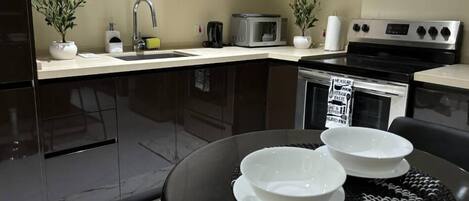 A modern kitchen with dark cabinets, a microwave, a stove, and a sink. There are two potted plants on the counter.