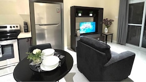Ein kompakter Wohnbereich mit Küchenzeile, einem Flachbildfernseher, einer Couch und einem Esstisch mit Tellern und Blumen.