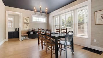 A dining area with a dark ceiling, wooden dining table, and chairs. There are framed pictures on the walls and a window with blinds.