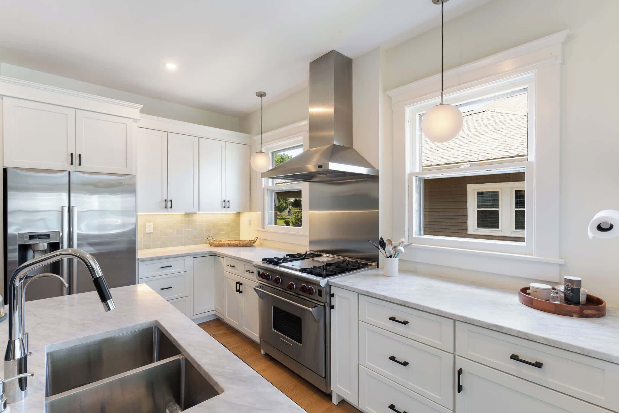 A modern kitchen with stainless steel appliances, white cabinetry, and a large window providing natural light.