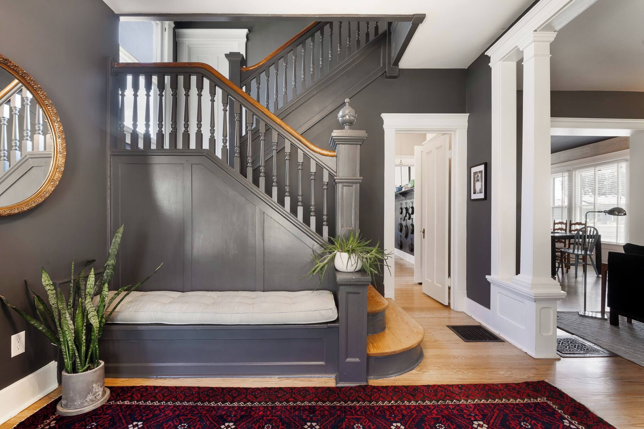 A staircase with dark wood railings and a white balustrade, leading to a landing with a bench and potted plants.