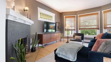 A living room with a fireplace, a sofa, a TV, and large windows with blinds.