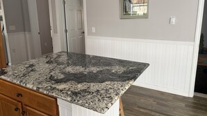 Una cocina con encimera de granito, armarios de madera, una puerta blanca y un cuadro en la pared.