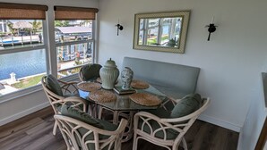 Een eethoek met rieten stoelen en een glazen tafel, met uitzicht op een waterpartij.