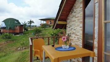 Une petite terrasse extérieure avec une table et des chaises, un vase de fleurs et une vue sur une colline parsemée de bâtiments.