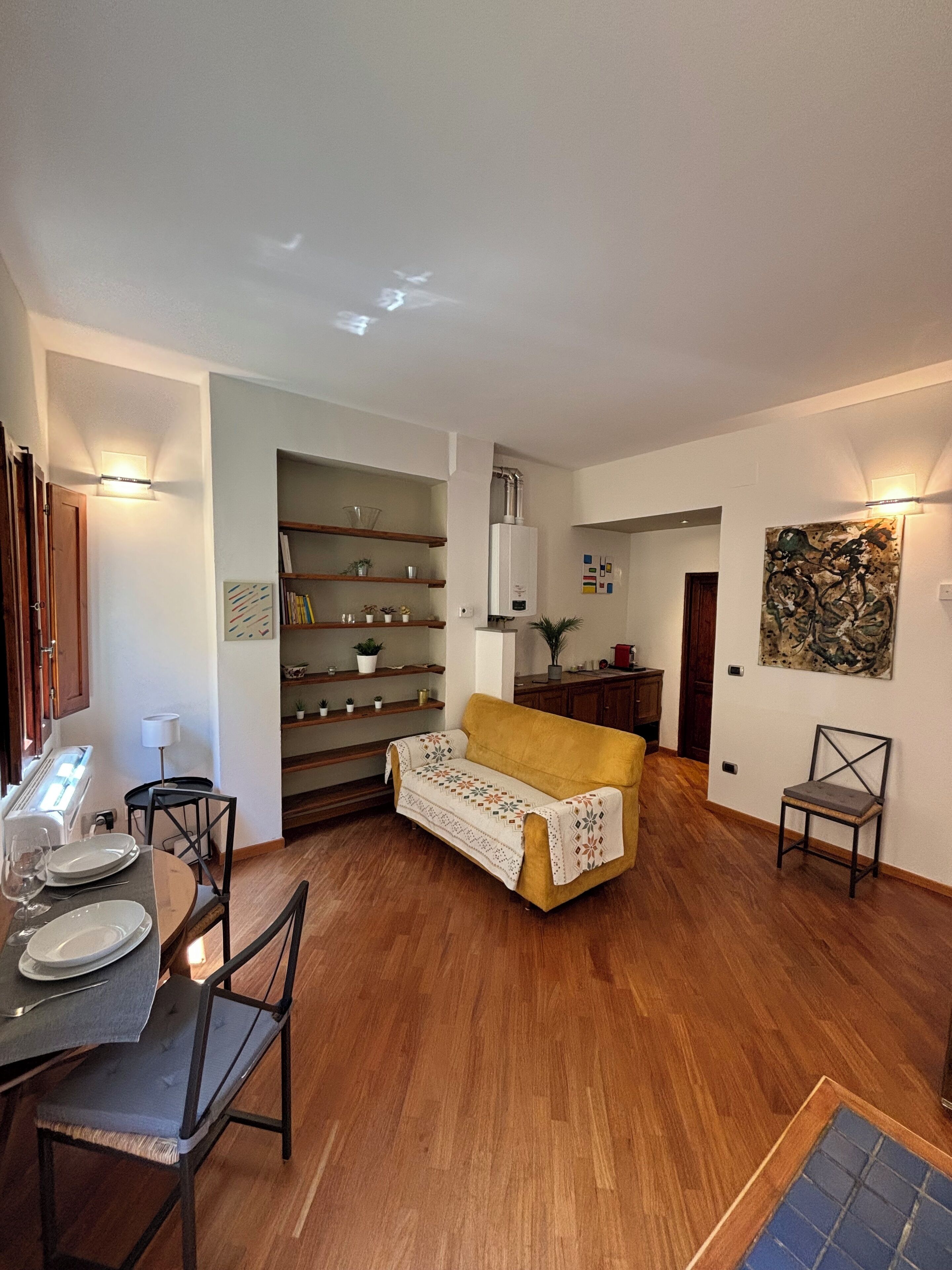 Un espacio habitable compacto con zona de comedor, sofá y cocina con estantes y radiador.