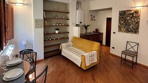 A compact living space with a dining area, a sofa, and a kitchen area with shelves and a radiator.