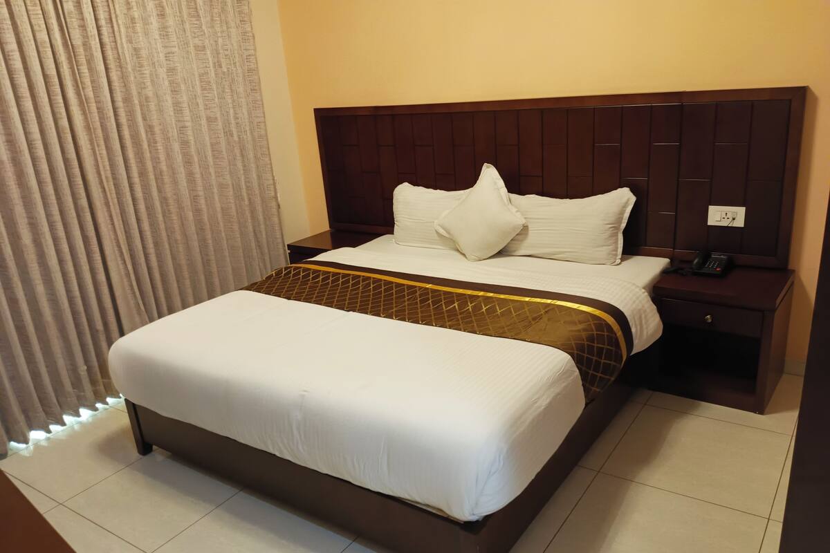 A hotel room with a large bed, a wooden headboard, a nightstand with a phone, and a curtain.