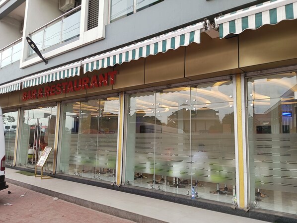 A bar and restaurant with a striped awning and large glass windows. - Hotel Indigo (Kinshasa)