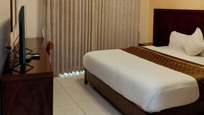 A hotel room with a bed, a desk with a television, an air conditioner, and a curtain. - Hotel Indigo (Kinshasa)