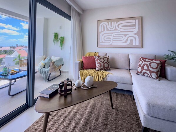 A modern living room with a sofa, coffee table, and a view of the cityscape through large windows. - Fantastic new Penthouse w/ private rooftop (Punta Cana)