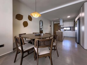 A modern kitchen with white cabinets, a central island, and a dining area with a round table and wooden chairs. - Fantastic new Penthouse w/ private rooftop (Punta Cana)