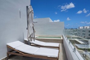 A rooftop lounge area with two sunbeds, a glass balustrade, and a view of the cityscape.