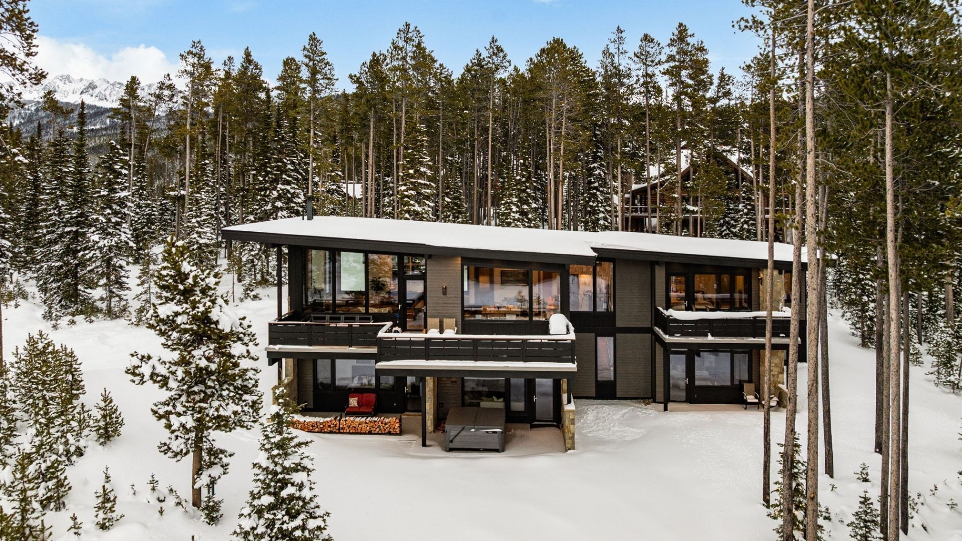 A modern, multi-story cabin with a large balcony, surrounded by a snowy forest.