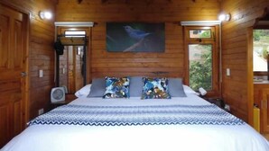A wooden cabin bedroom with a bed, pillows, a painting, and a window. - Romantic Cabin with Jacuzzi Azulejo (Acacías)
