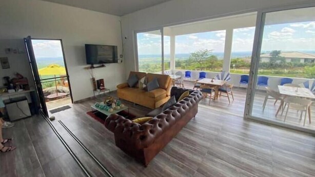 A spacious living room with a large sofa, a coffee table, and a TV. There is a balcony with outdoor seating and a view of the landscape. - Romantic Cabin with Jacuzzi Azulejo (Acacías)