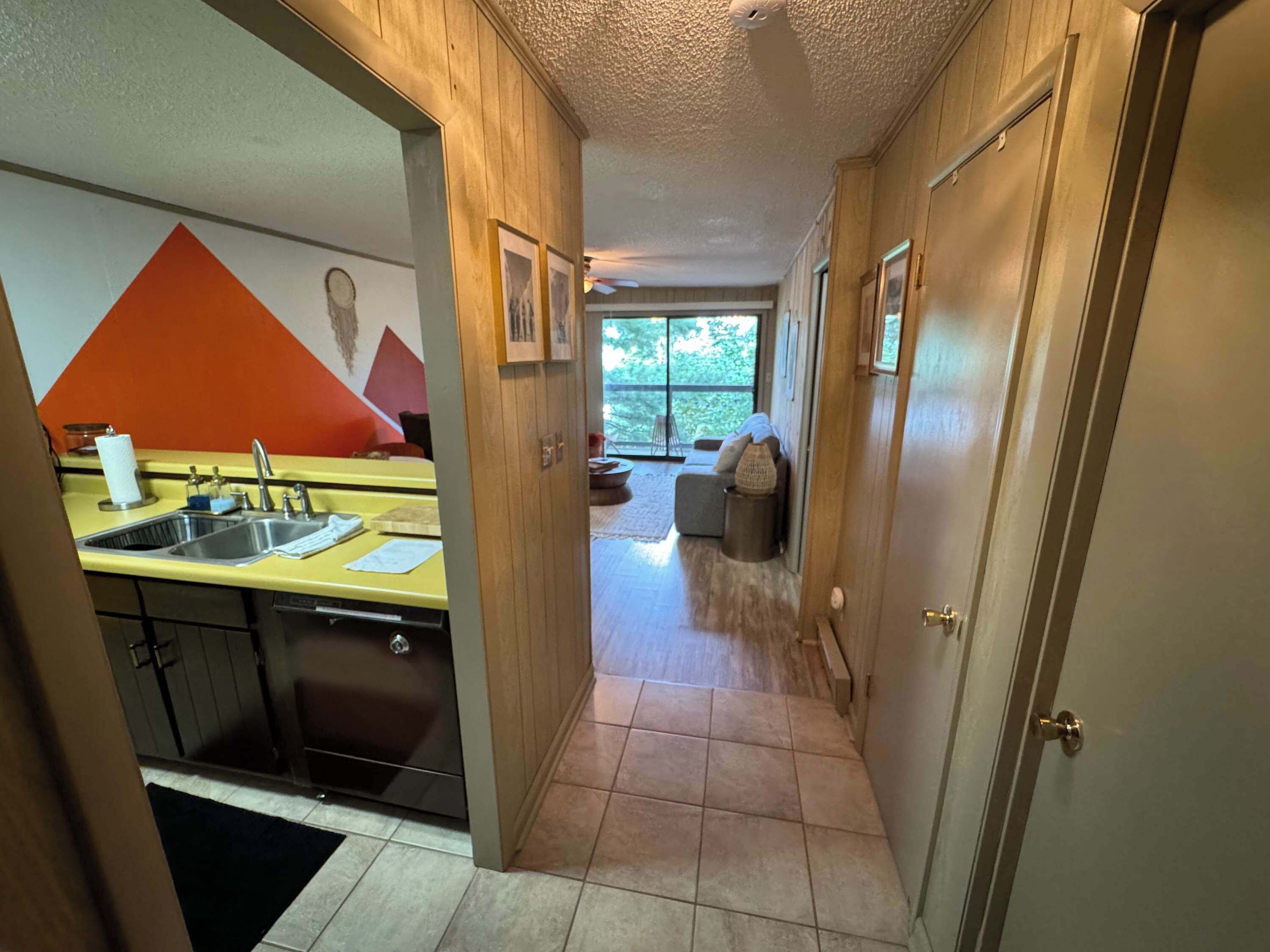 A narrow hallway leading to a kitchen with a sink and a dining area with a table and chairs.