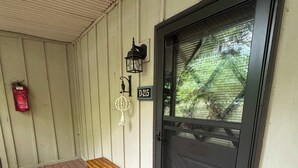 Une véranda en bois avec un banc, une porte noire dotée d’un panneau de verre, une lanterne et une boîte aux lettres.