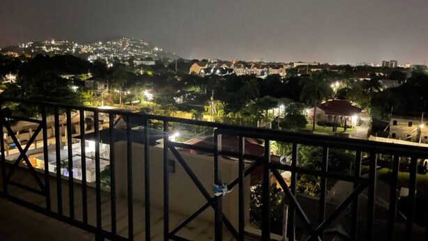 Vista notturna da un balcone con ringhiera, affacciata su una zona residenziale con case e lampioni.