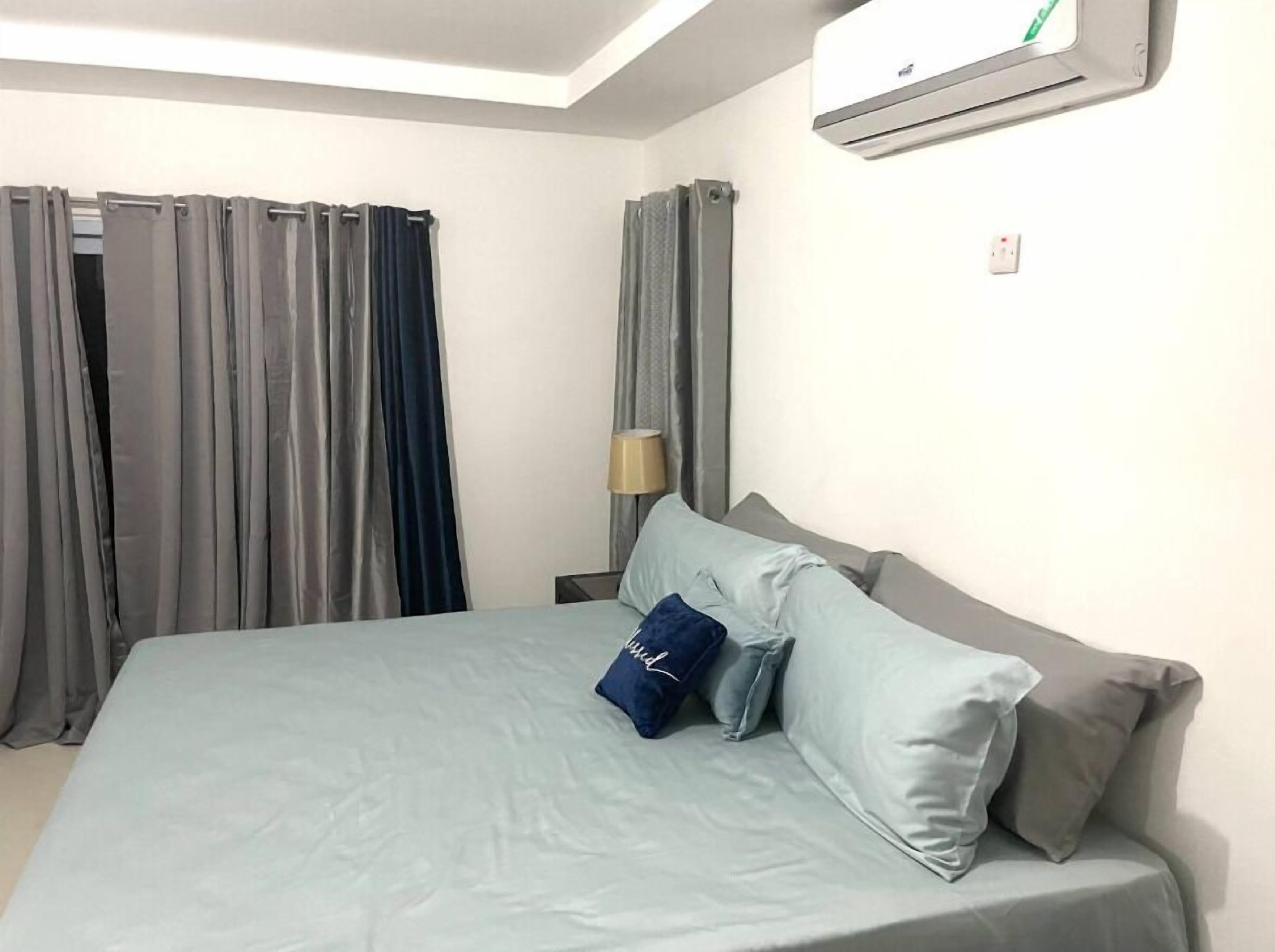 A hotel room with a bed, curtains, a lamp, and an air conditioning unit.