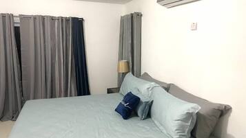 A hotel room with a bed, curtains, a lamp, and an air conditioning unit.