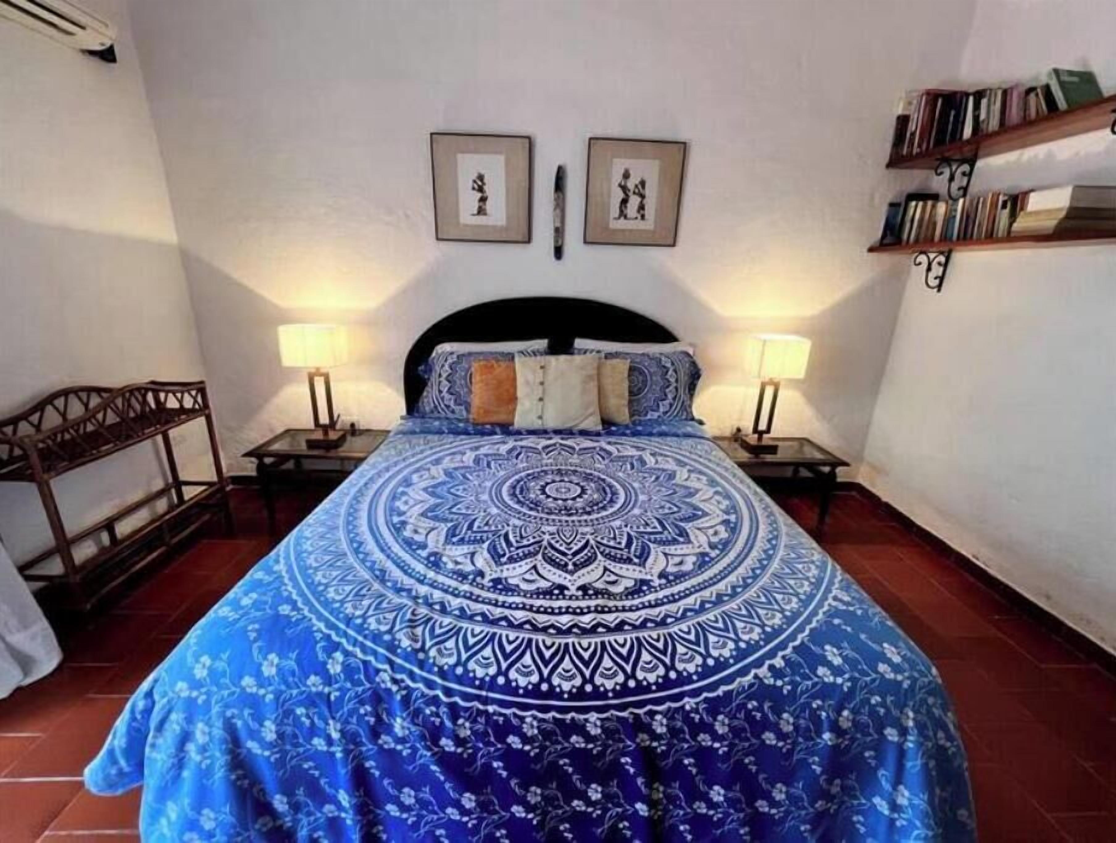 Een slaapkamer met een groot bed, twee nachtkastjes, een houten bankje en een boekenkast.