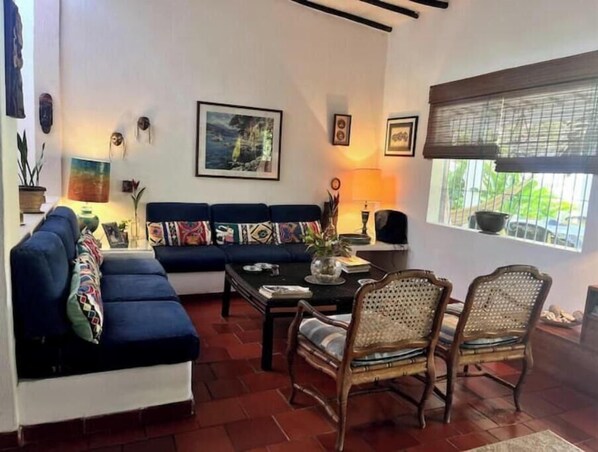 A living room with a blue sofa, two wicker chairs, a coffee table, and a window with blinds.