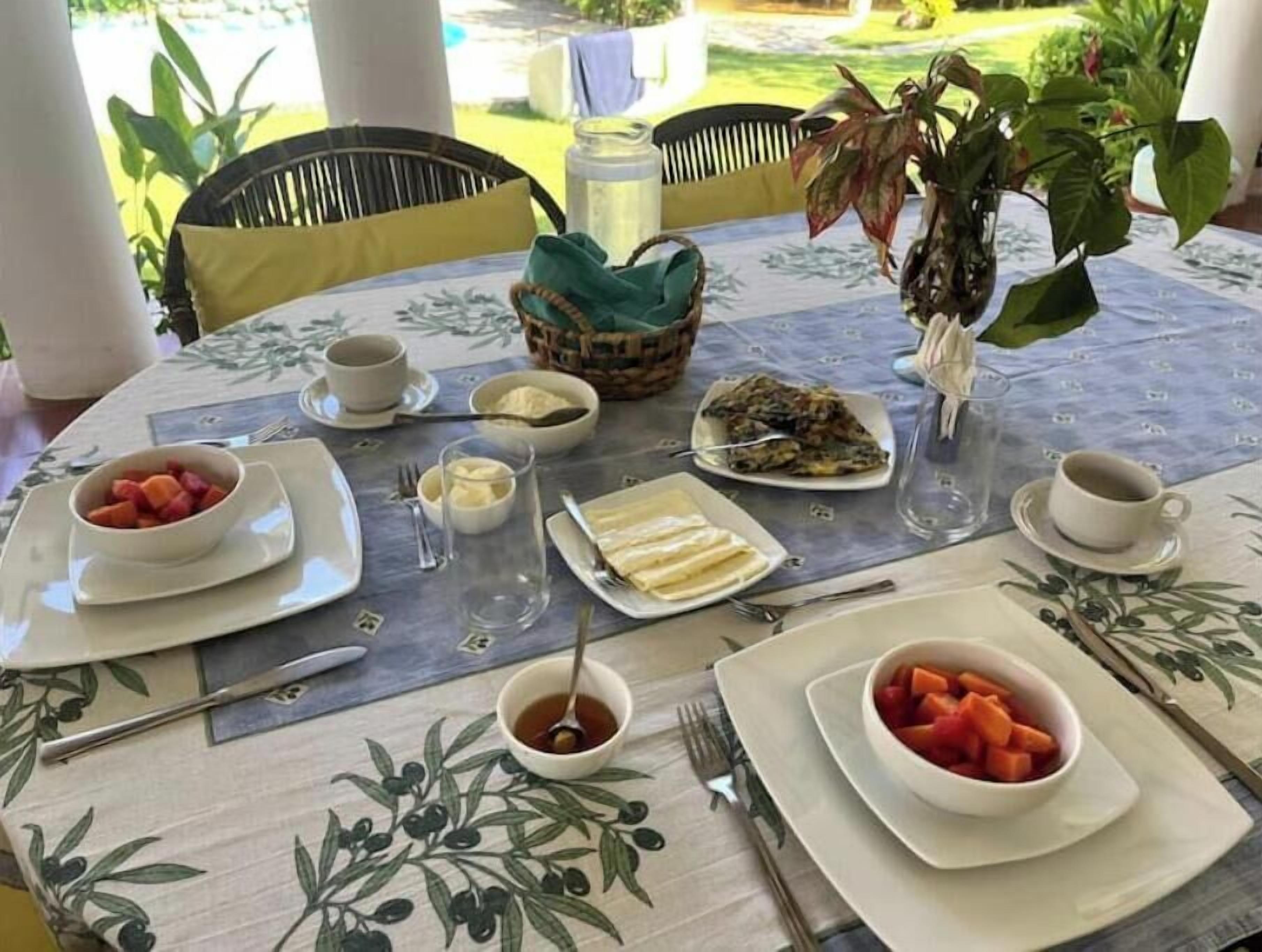 Una mesa preparada para el desayuno con diversos platos, como fruta, pan y una bebida caliente.