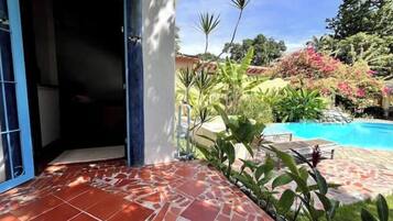 Un pati amb rajoles i una piscina, envoltat de vegetació abundant i un cel blau clar.