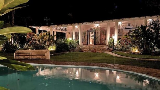 A pool area with a well-lit building in the background, surrounded by lush greenery. - Beautiful room in Choroni (Puerto Colombia 2110)