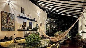 An outdoor dining area with a glass table and chairs, surrounded by plants and a hammock. - Beautiful room in Choroni (Puerto Colombia 2110)