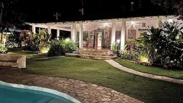 A poolside area with a stone border, a well-maintained lawn, and a building with a covered patio and steps leading to the entrance.
