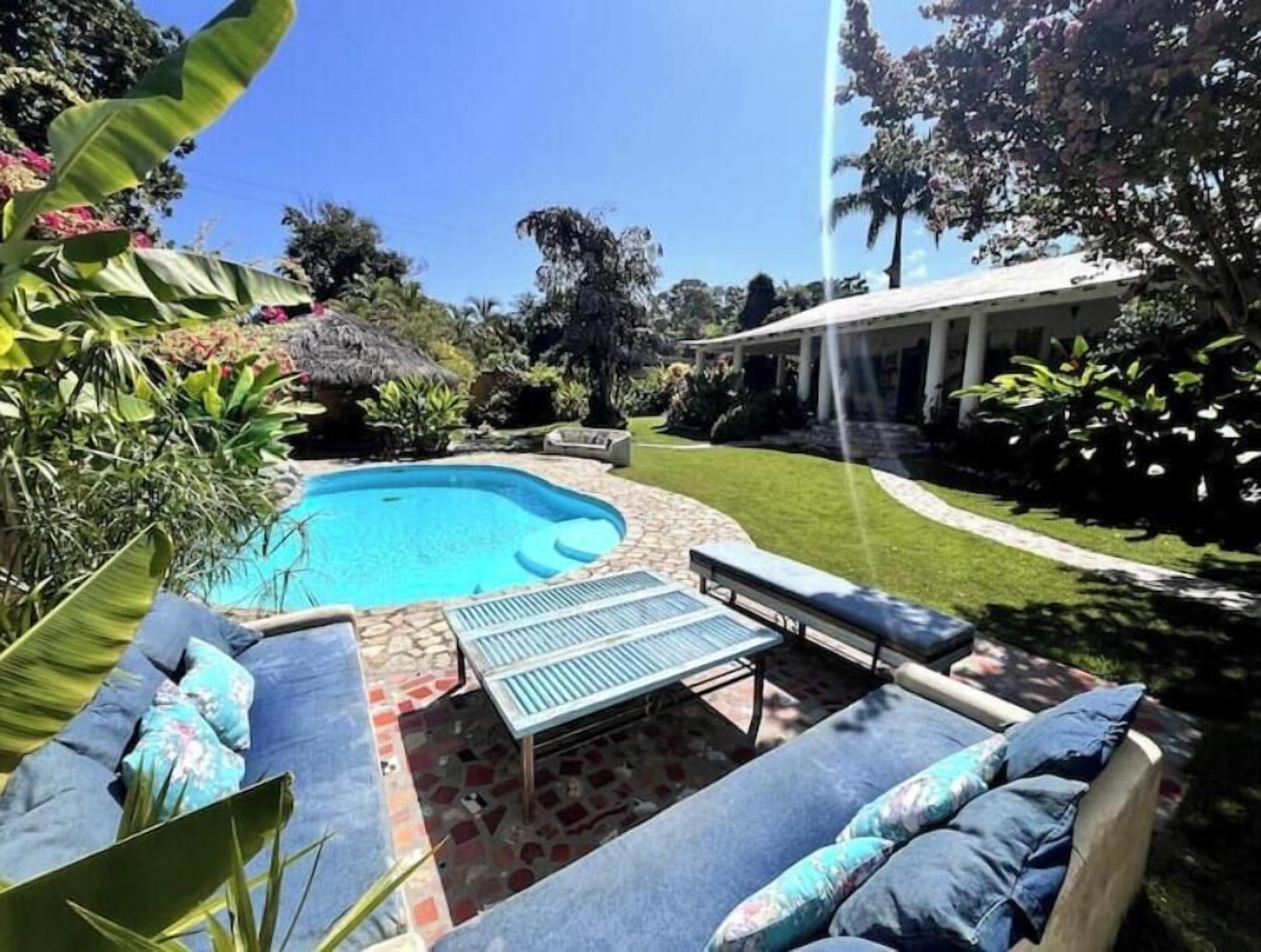 A backyard with a swimming pool, a covered patio area, and a lawn.