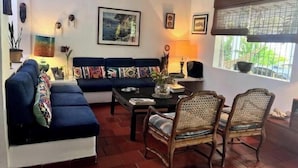 A living room with a blue sofa, two wicker chairs, a coffee table, and a window with blinds. - Room for a couple in Choroni (Puerto Colombia 2110)
