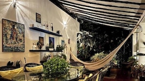 An outdoor dining area with a glass table and chairs, surrounded by plants and a hammock. - Room for a couple in Choroni (Puerto Colombia 2110)