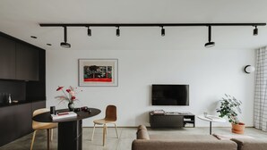 A modern living room with a black dining table, a sofa, a TV, and a plant.