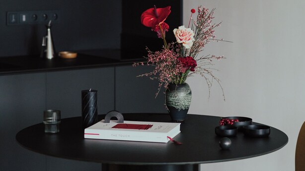 A modern kitchen with dark cabinetry, a round black table, and a vase with flowers.