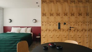 A hotel room with a bed, a wooden wardrobe, a round table with bowls, and a chair.