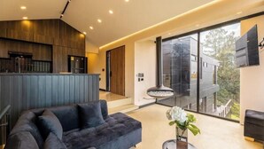 Una sala moderna con un sofá oscuro, una mesita auxiliar con un jarrón y un ventanal que ofrece vistas al exterior.