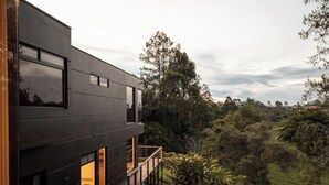 Un edificio moderno con amplios ventanales y un balcón con vistas a un paisaje exuberante y verde.